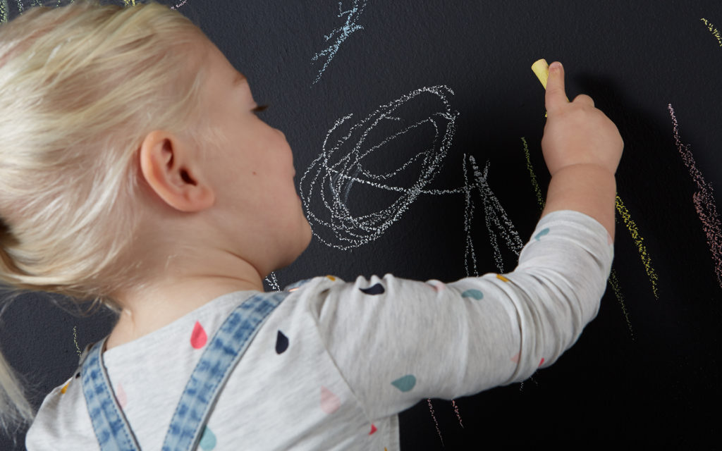 Писанные мелом. Видеть мелом. Рисование грифельной крошкой в детском саду. Счастливый ребенок на фоне грифельной стены. Новые технологии мелом.